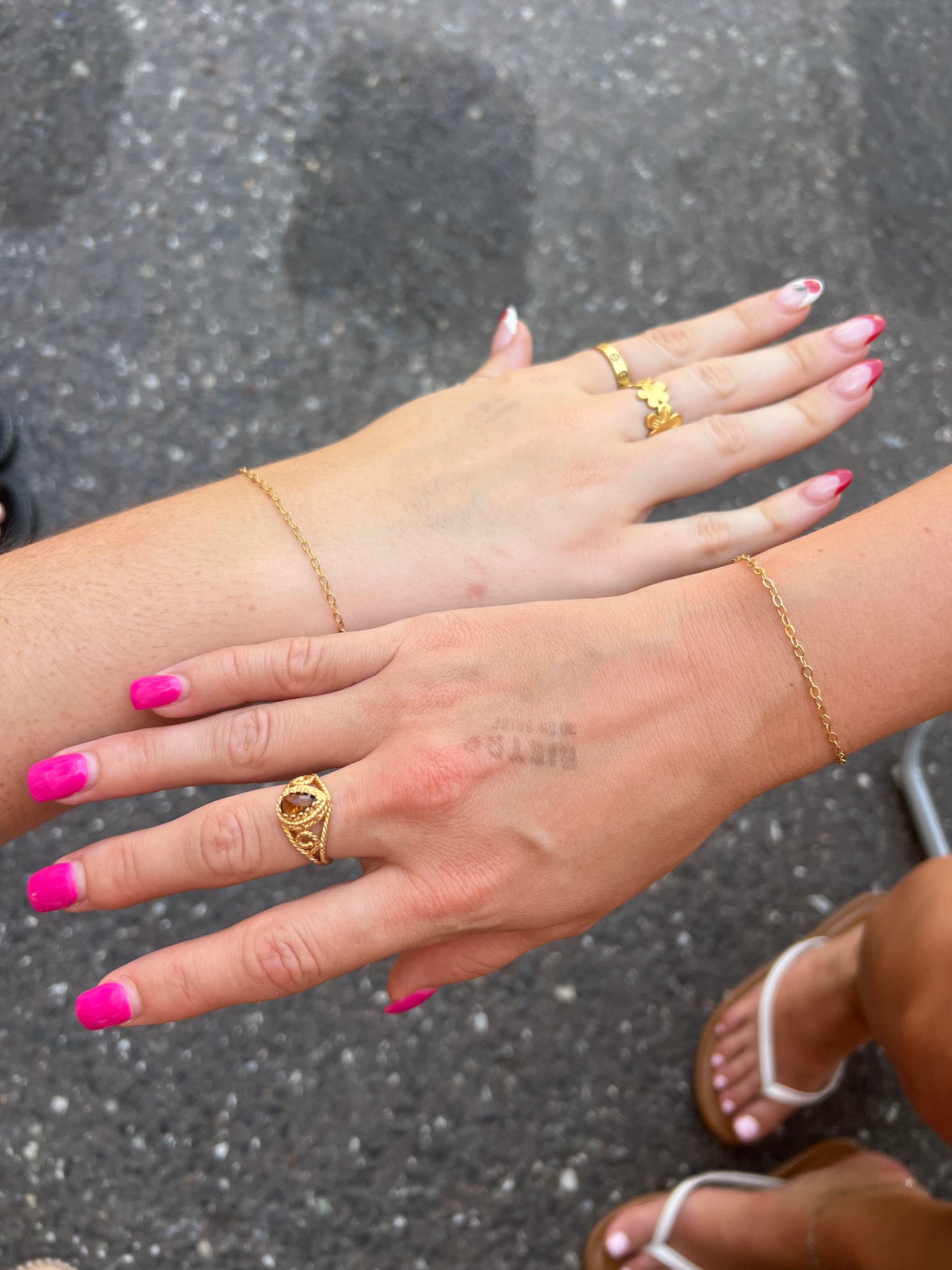close-up of hands with gold rings and pink nail polish on a dark background
