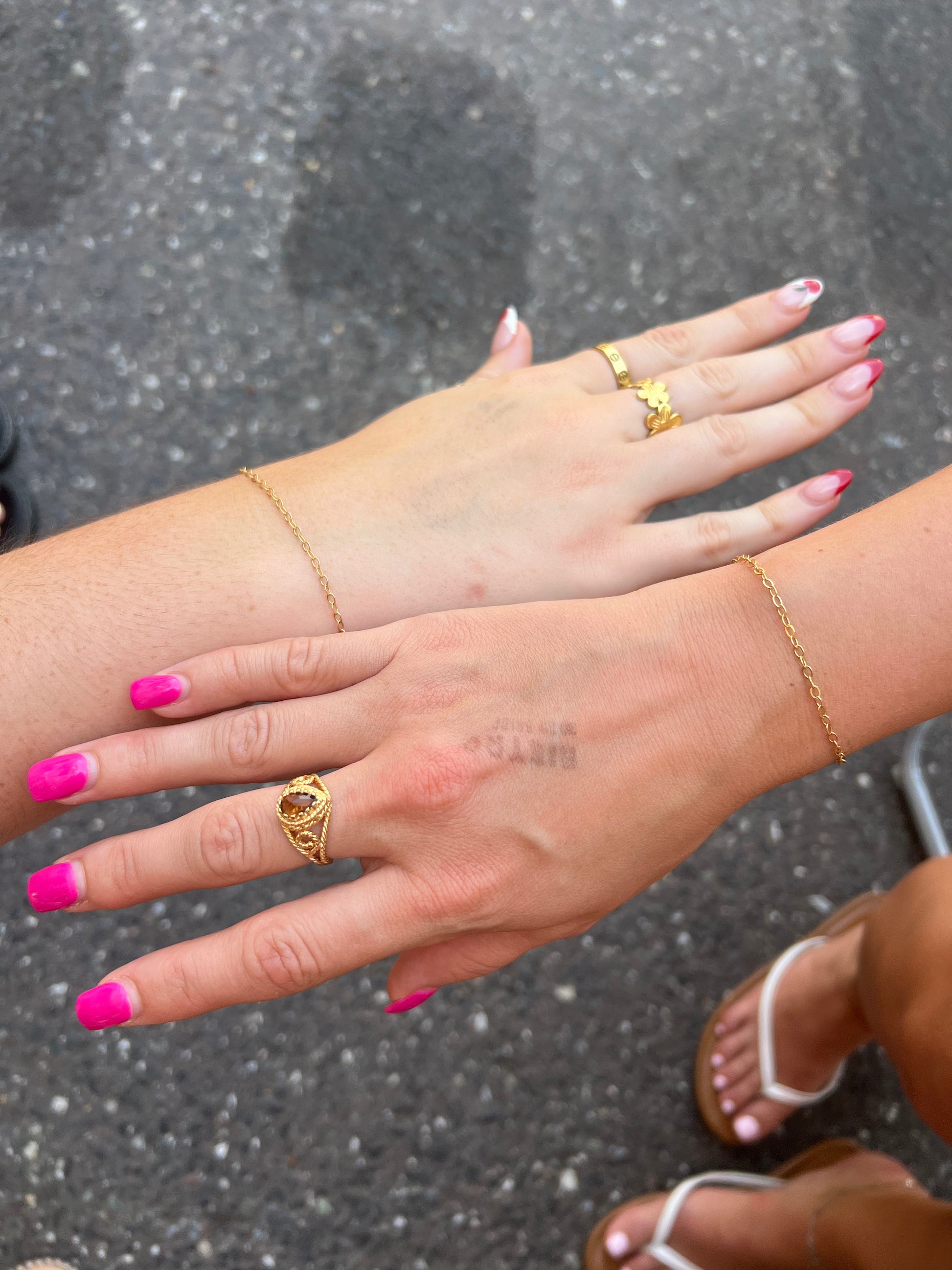 Close-up of hands with gold rings and pink nail polish on a dark background