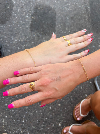 Close-up of hands with gold rings and pink nail polish on a dark background