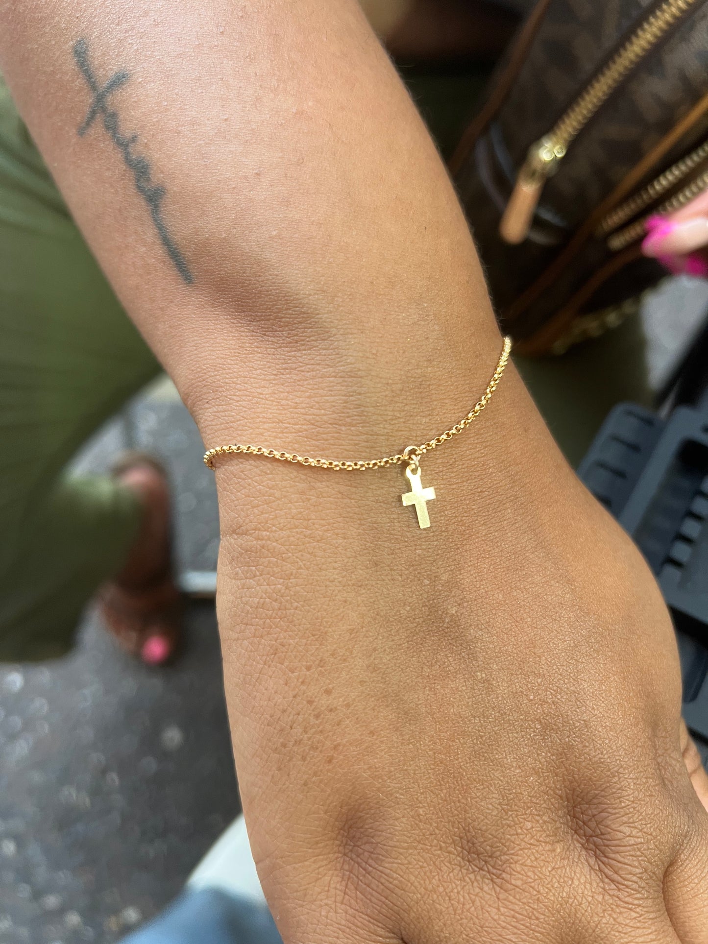 14k gold filled rolo chain bracelet with a cross on a wrist, with a blurred background